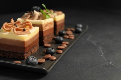 Pieces of triple chocolate mousse cake on black table, closeup with space for text