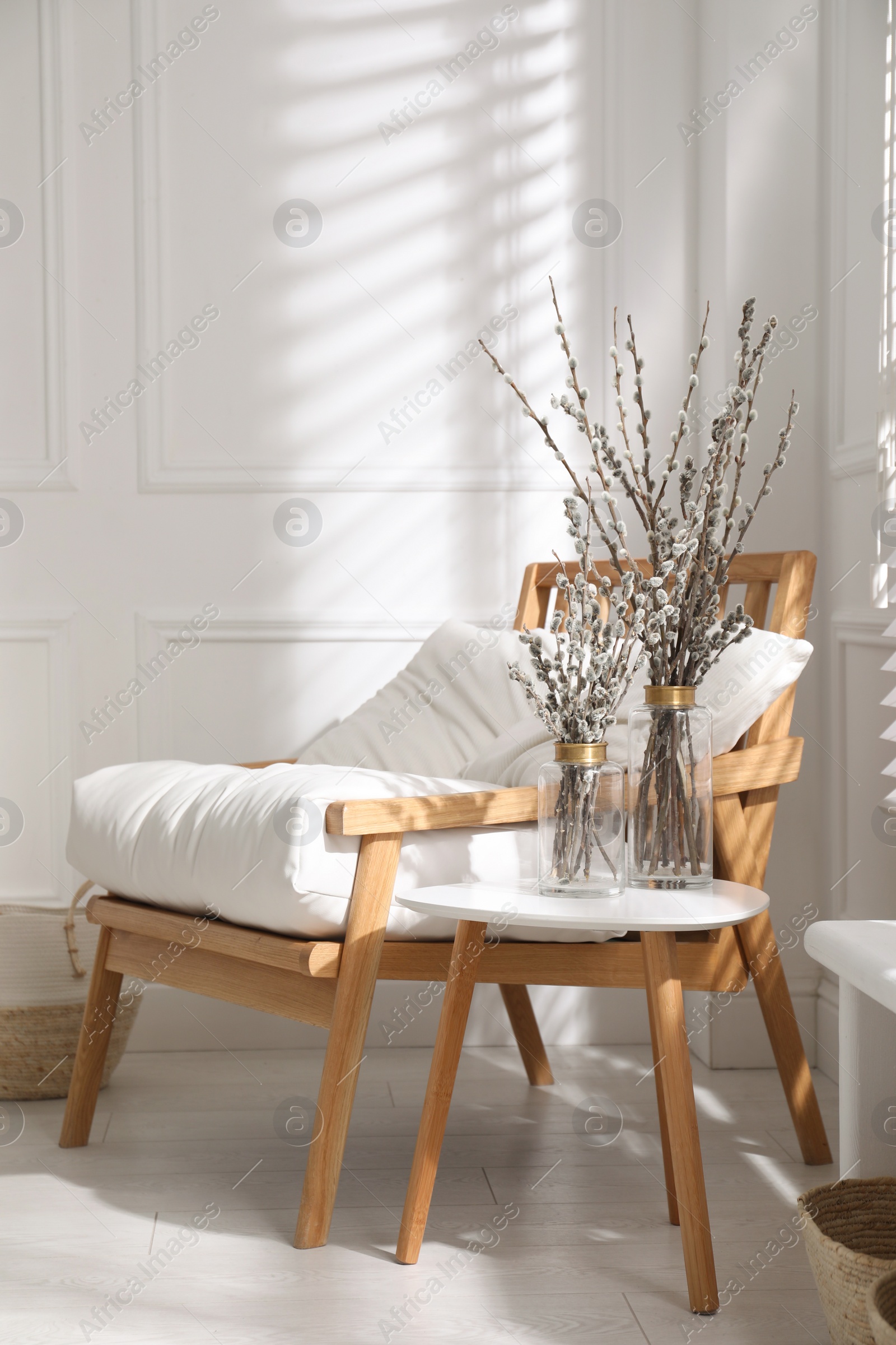 Photo of Glass vases with pussy willow tree branches on table near armchair in room