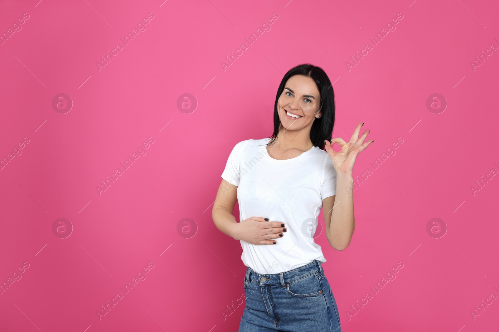 Photo of Happy woman touching her belly and showing okay gesture on pink background, space for text. Concept of healthy stomach