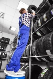 Young male mechanic with car tires in automobile service center