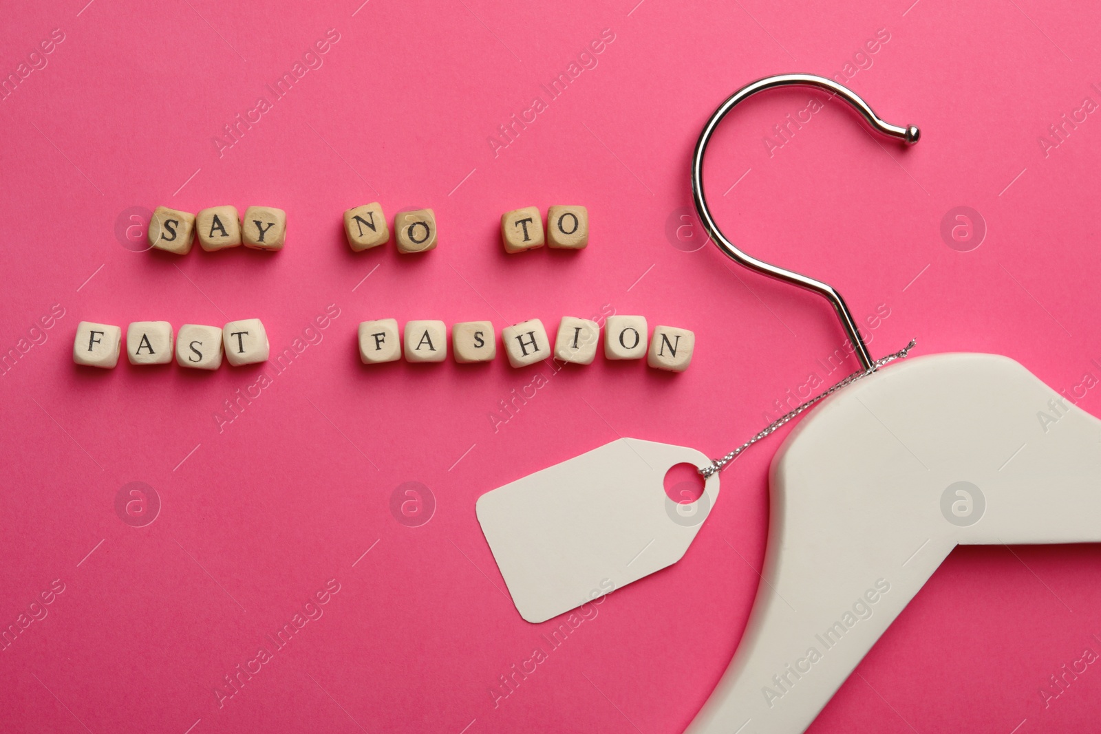 Photo of Wooden cubes with phrase SAY NO TO FAST FASHION, white hanger and tag on pink background, flat lay