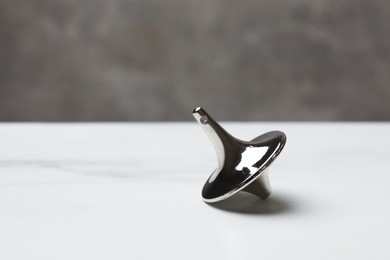 Photo of One metal spinning top on white table, closeup. Space for text