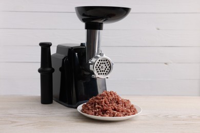 Photo of Electric meat grinder with beef mince on white wooden table