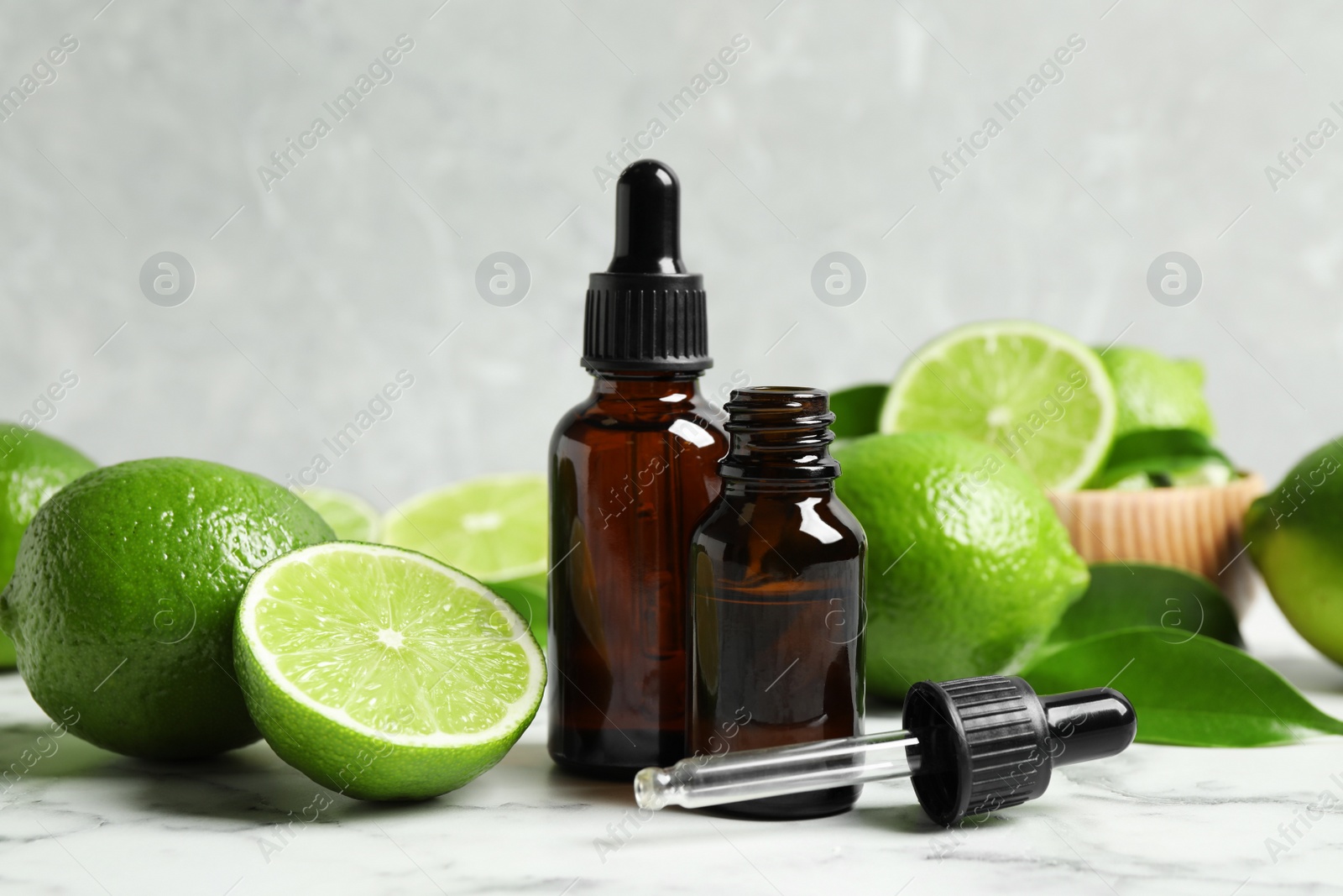 Photo of Lime essential oil and citrus fruits on marble table