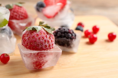 Ice cubes with different berries and mint on wooden board, closeup. Space for text