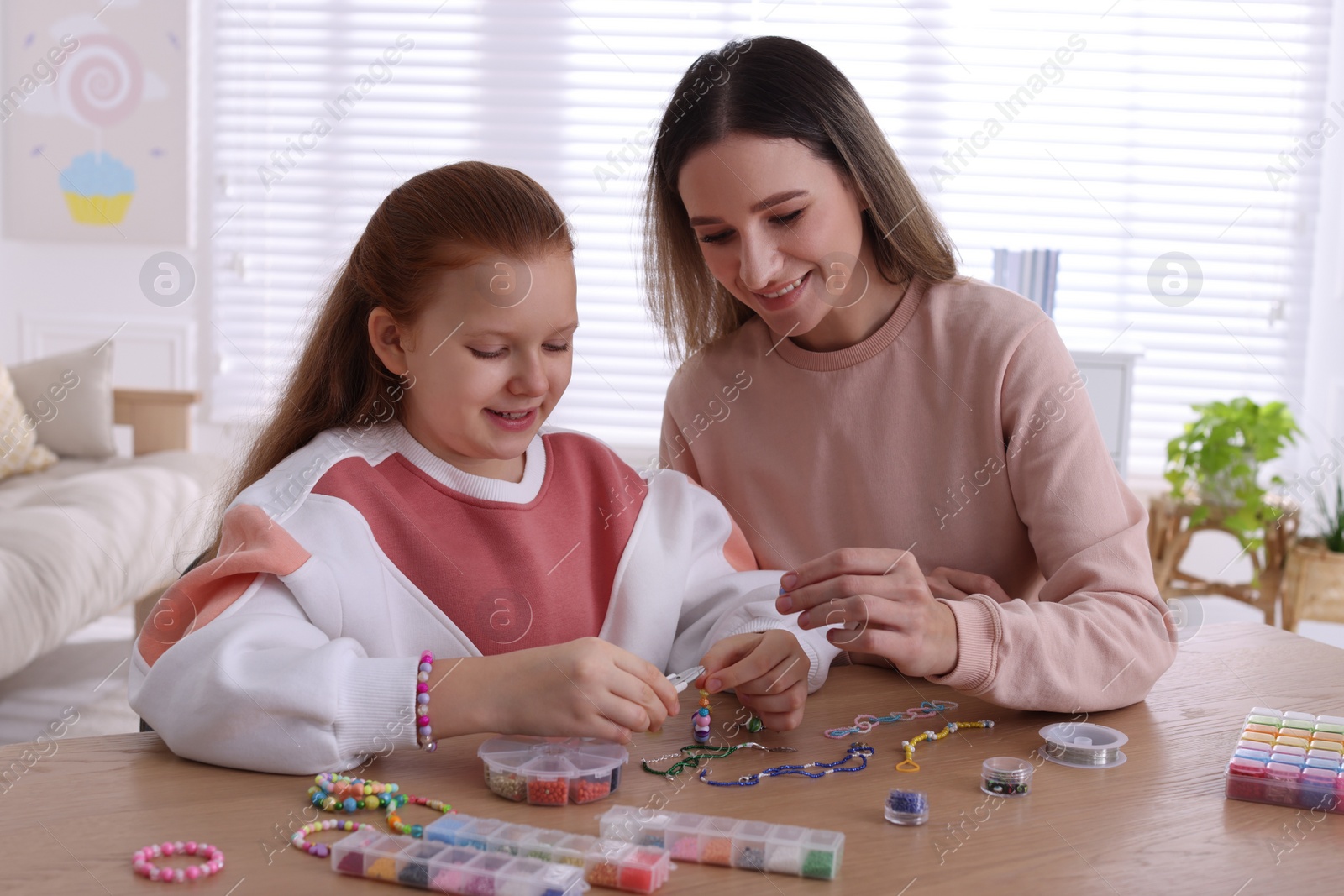 Photo of Happy mother with her daughter making beaded jewelry at home