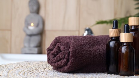 Rolled bath towel and different cosmetic products on table in bathroom, closeup