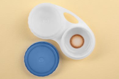 Case with color contact lenses on pale yellow background, flat lay