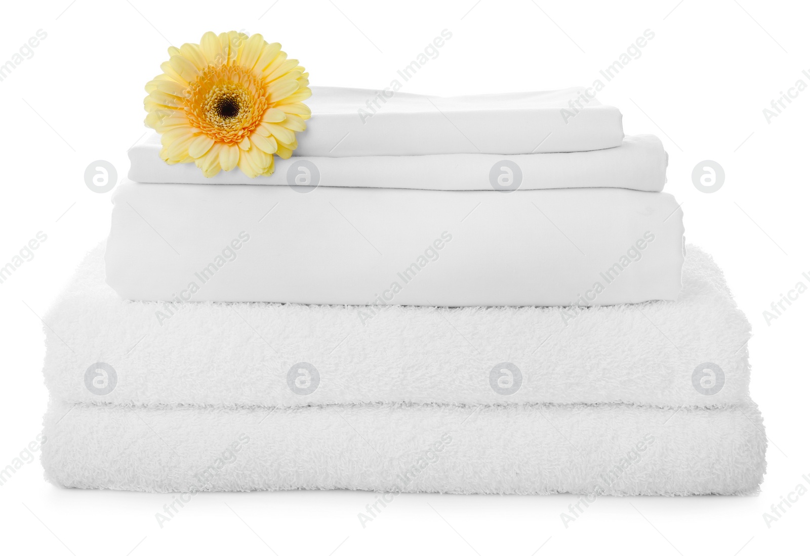 Photo of Stack of towels and bed sheets with gerbera on white background