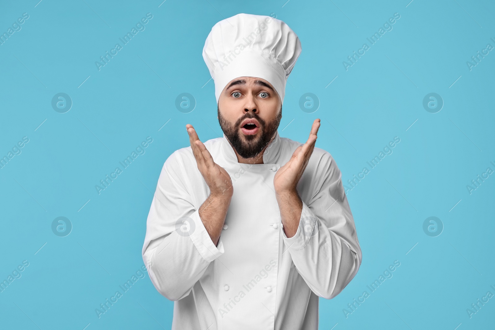 Photo of Surprised young chef in uniform on light blue background