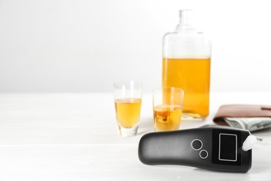 Modern breathalyzer and alcohol on white table. Space for text