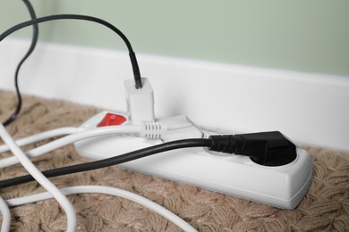 Photo of Power strip with different electrical plugs on floor indoors, closeup