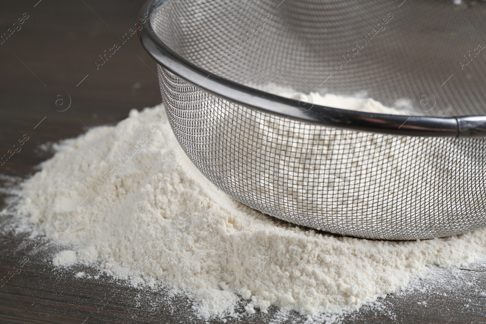 Photo of Metal sieve with flour on wooden table, closeup