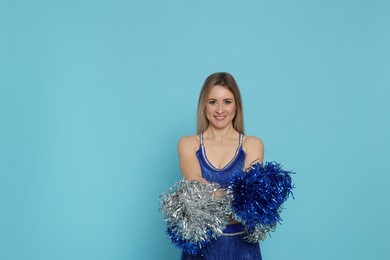 Photo of Beautiful cheerleader in costume holding pom poms on light blue background