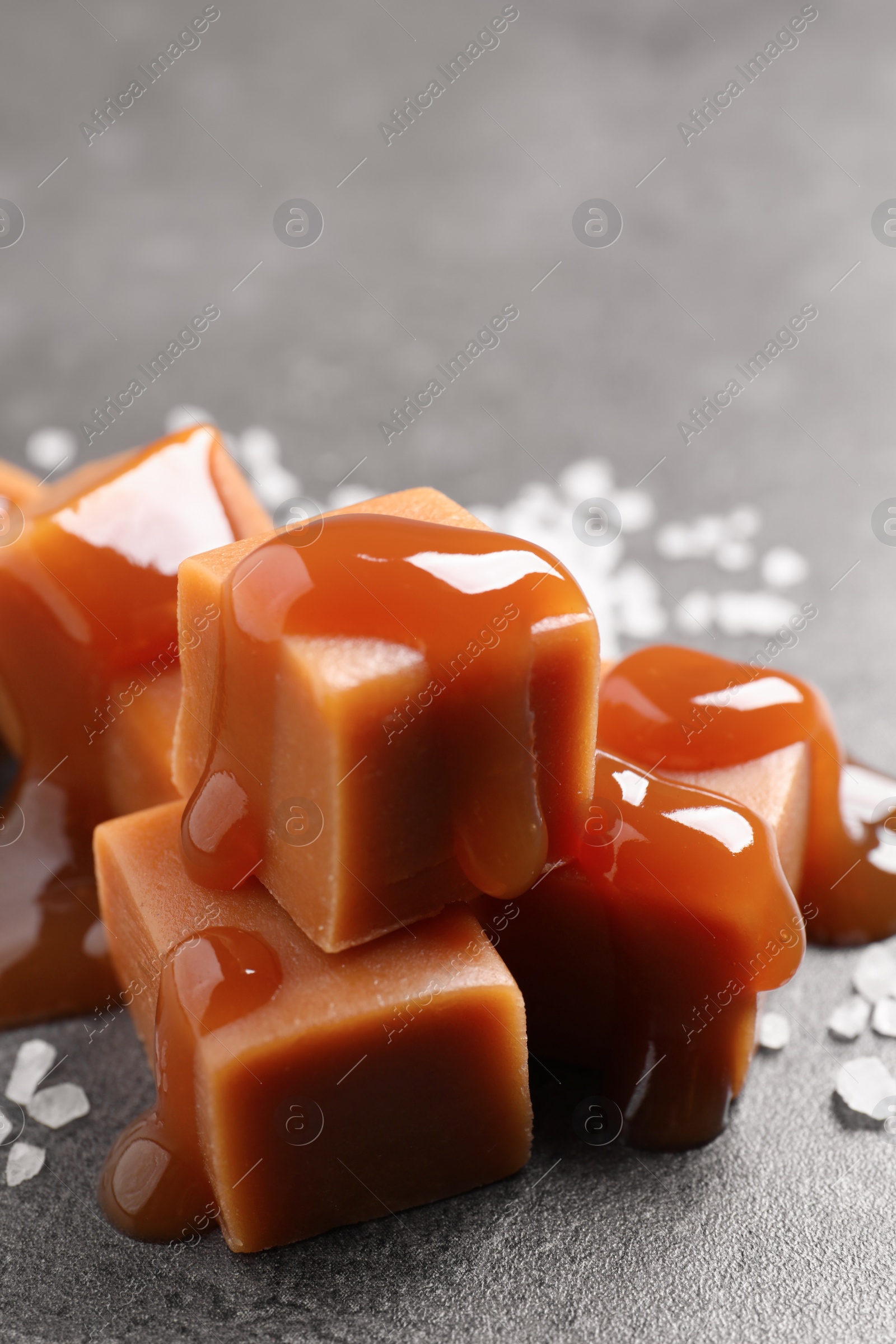 Photo of Yummy caramel candies with sauce and sea salt on grey table, closeup