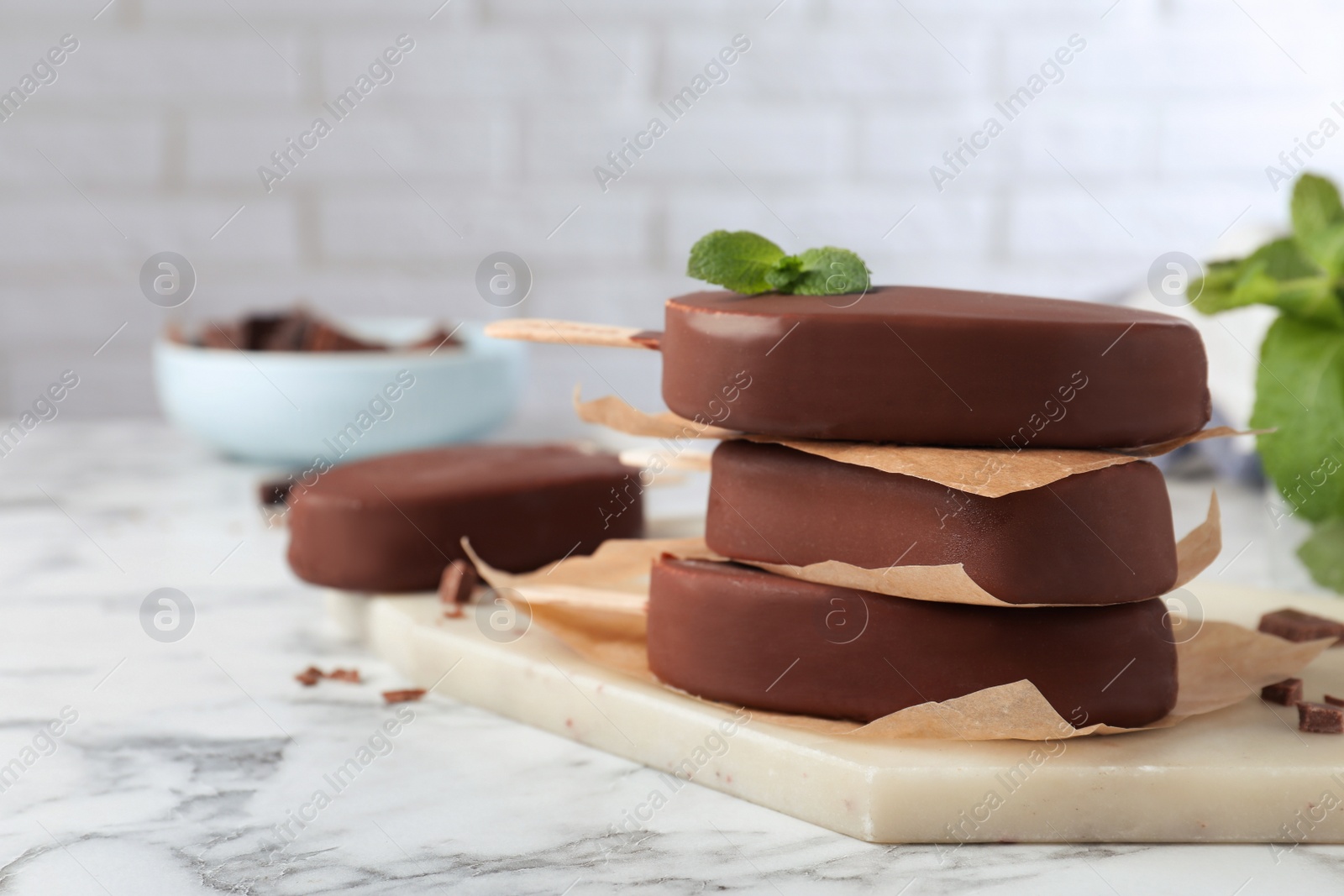 Photo of Delicious glazed ice cream bars with mint on white marble table.  Space for text