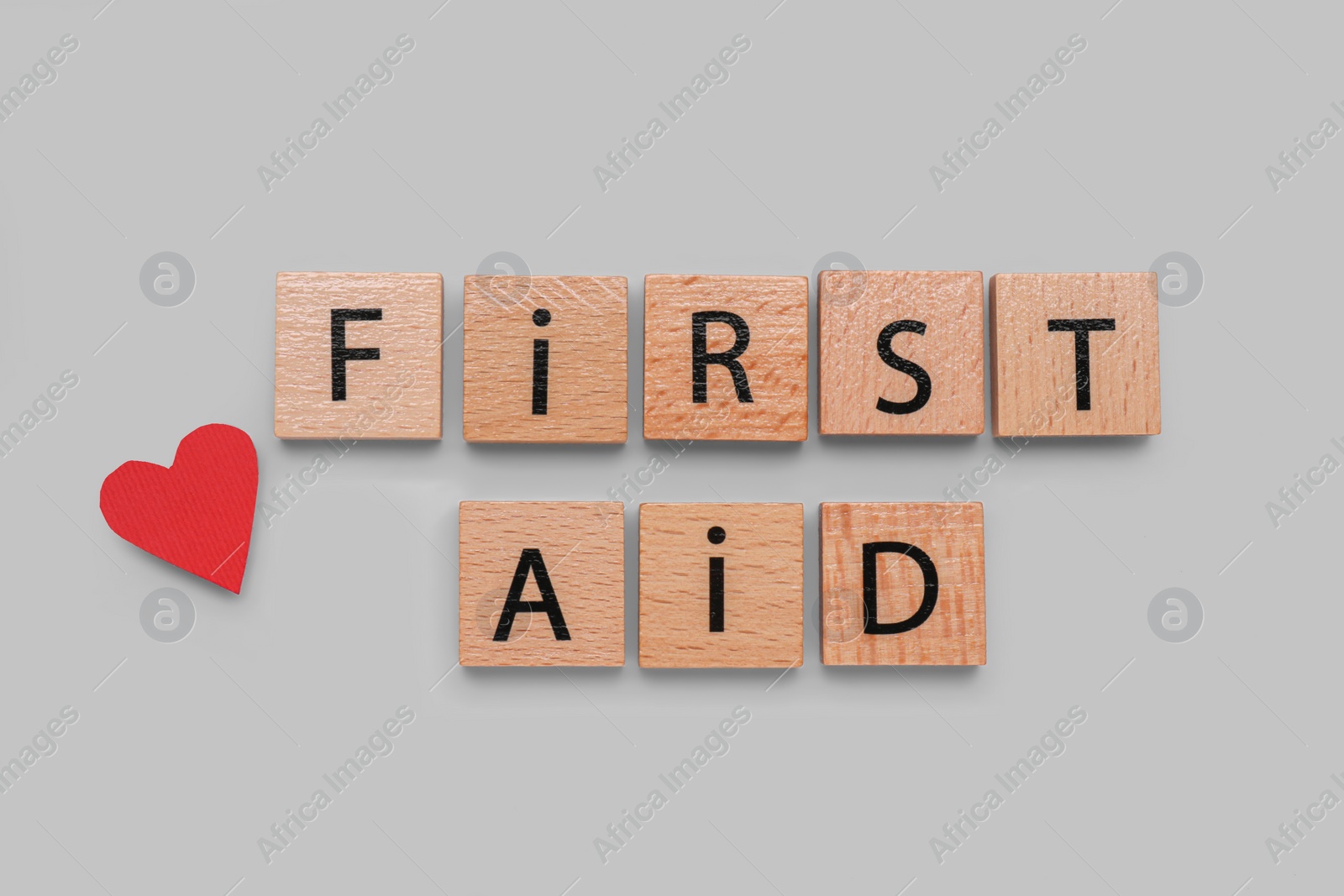 Photo of Words First Aid made of wooden cubes and cardboard heart on grey background, flat lay