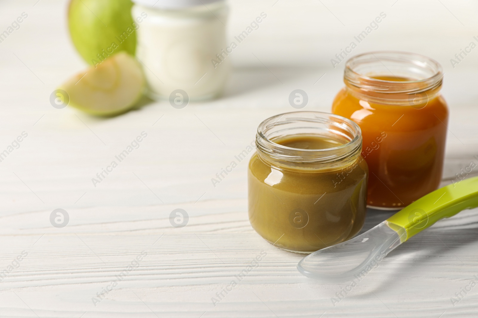 Photo of Jars with healthy baby food and spoon on white wooden table. Space for text