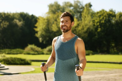 Man practicing Nordic walking with poles in park on sunny day