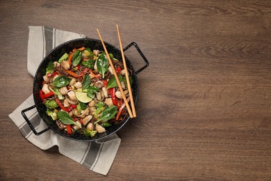 Photo of Stir-fry. Tasty noodles with meat in wok and chopsticks on wooden table, top view. Space for text