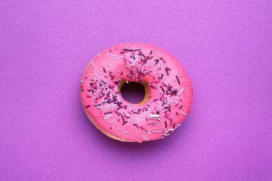 Photo of Sweet glazed donut decorated with sprinkles on purple background, top view. Tasty confectionery