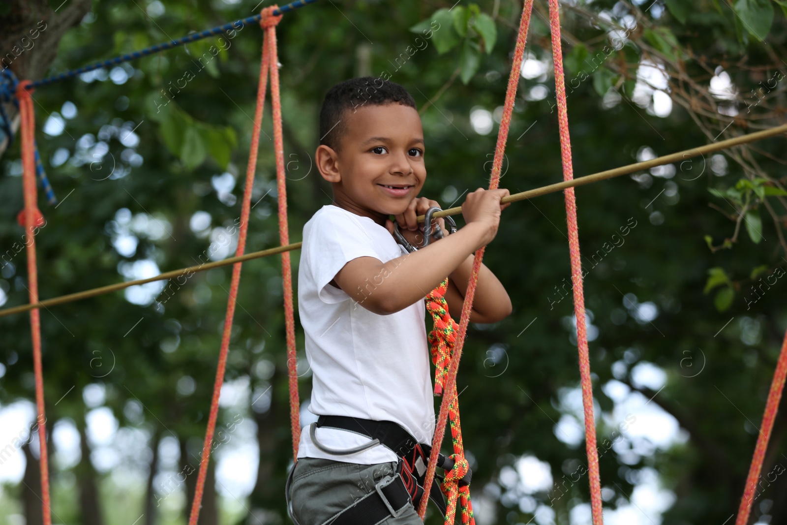 Photo of Little African-American boy climbing in adventure park. Summer camp