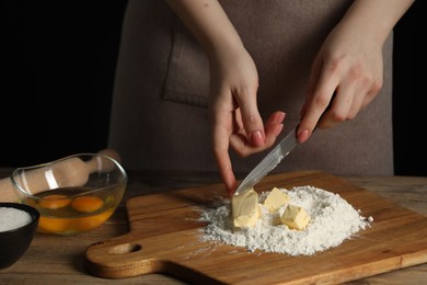 Photo of Woman cutting fresh butter at wooden table, closeup