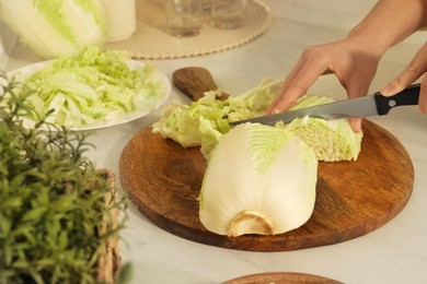 Photo of Woman cutting fresh chinese cabbage at kitchen table, closeup