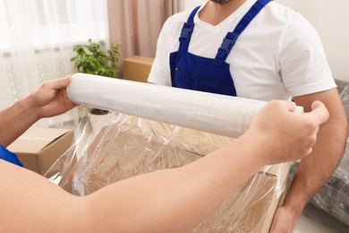 Photo of Workers wrapping box in stretch film indoors, closeup