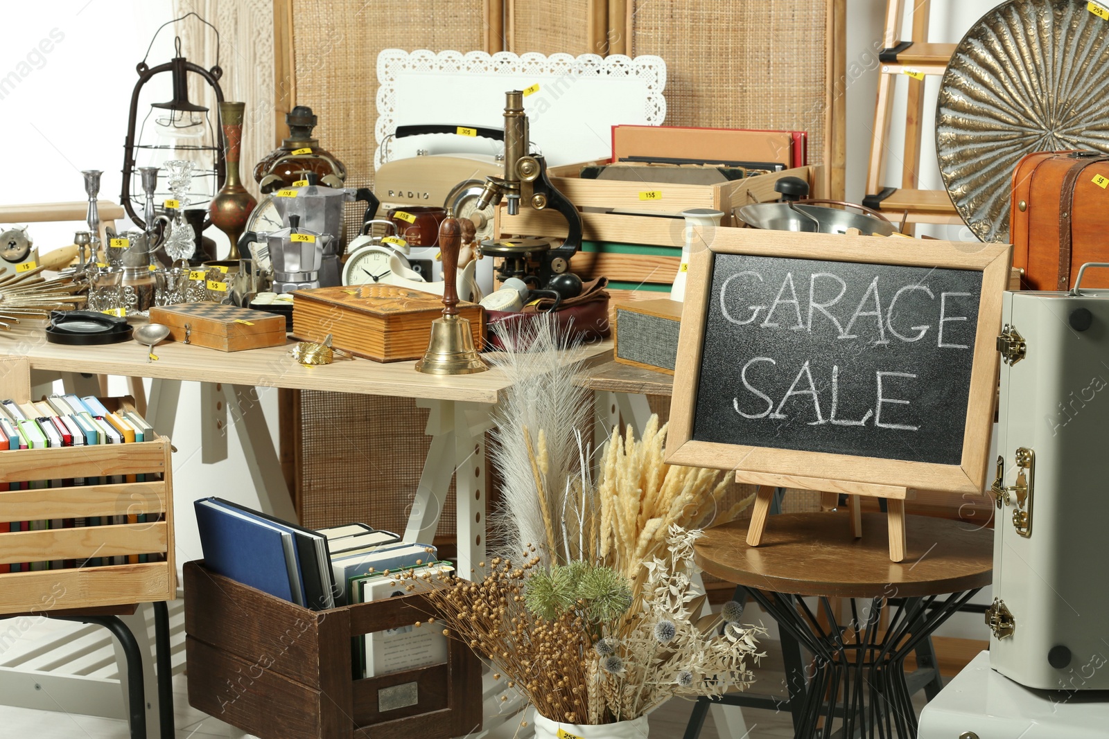 Photo of Sign Garage Sale written on blackboard near many different stuff indoors