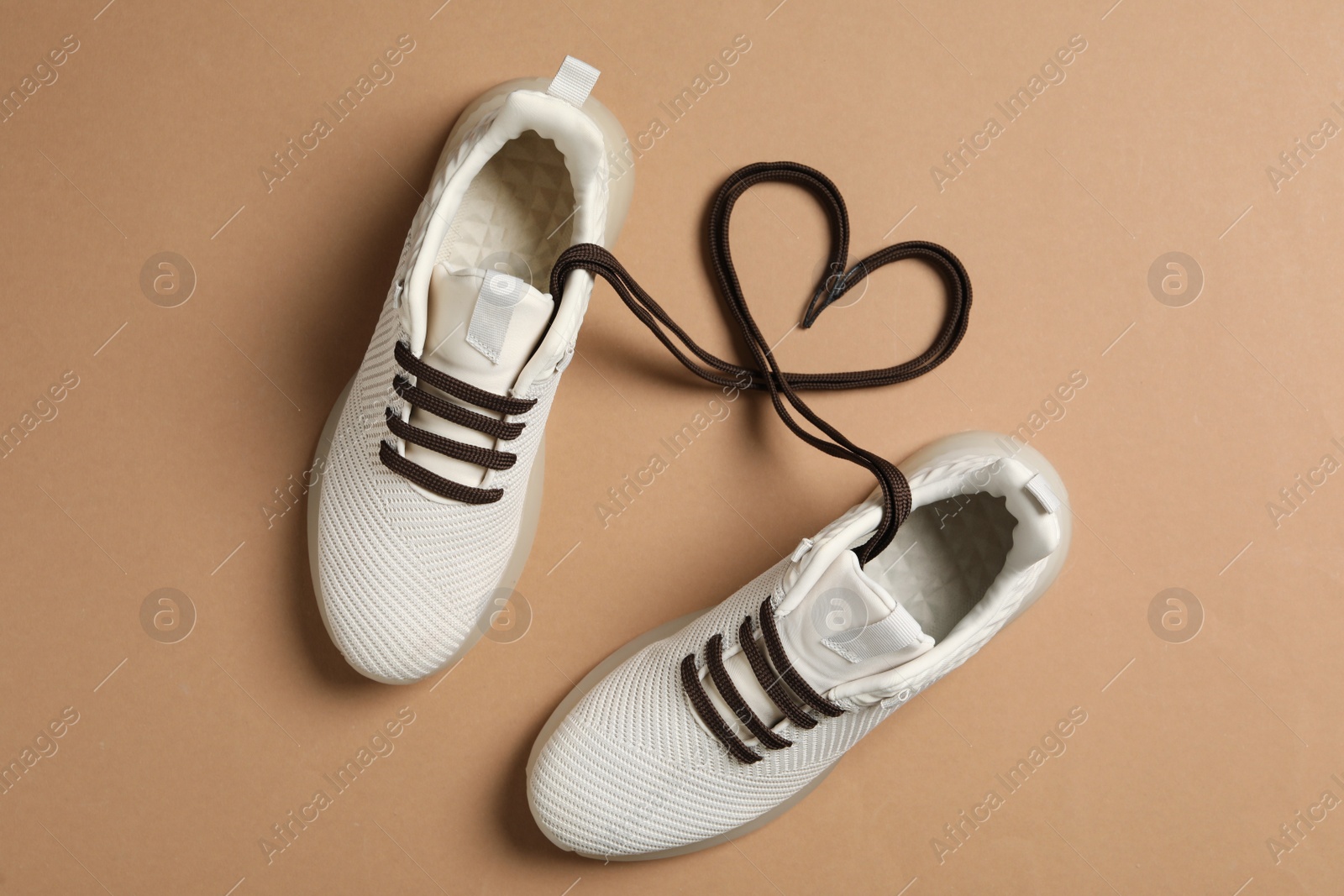 Photo of Stylish sneakers and shoe laces in shape of heart on brown background, flat lay