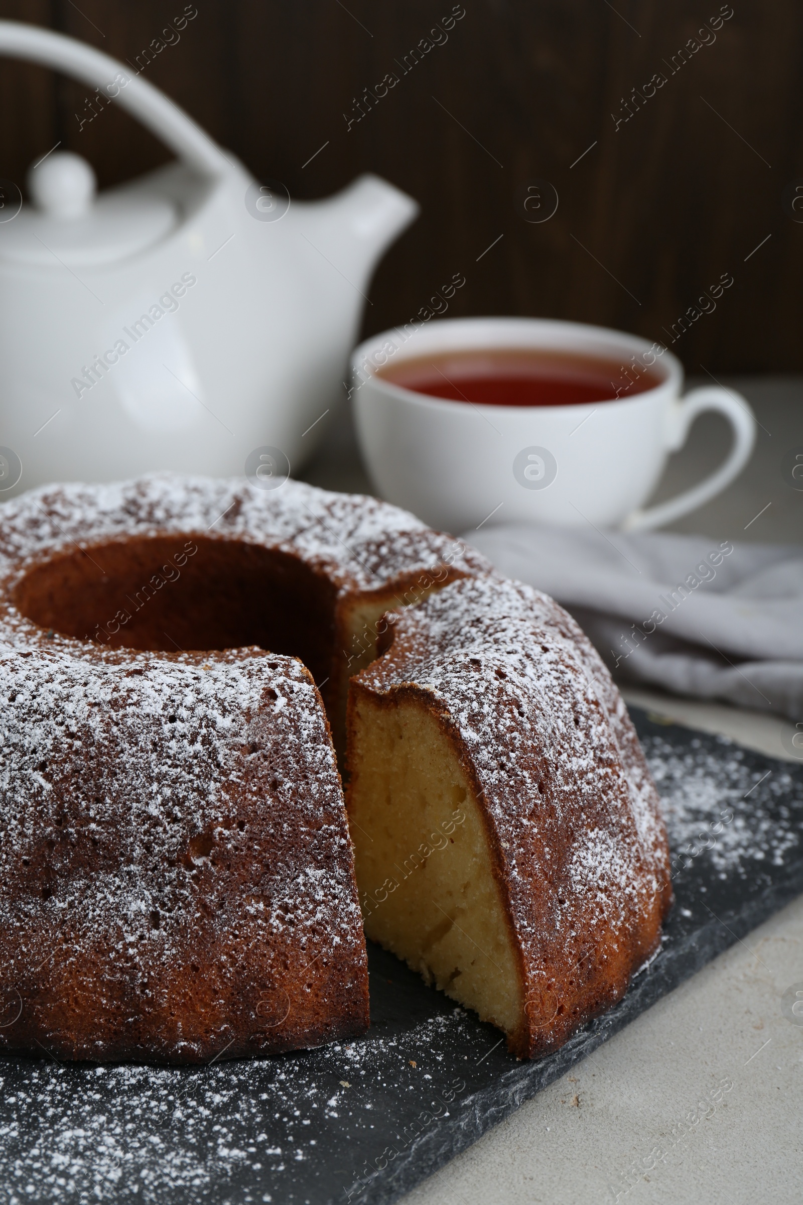 Photo of Homemade yogurt cake with powdered sugar on light grey table, closeup