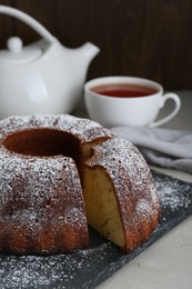 Photo of Homemade yogurt cake with powdered sugar on light grey table, closeup