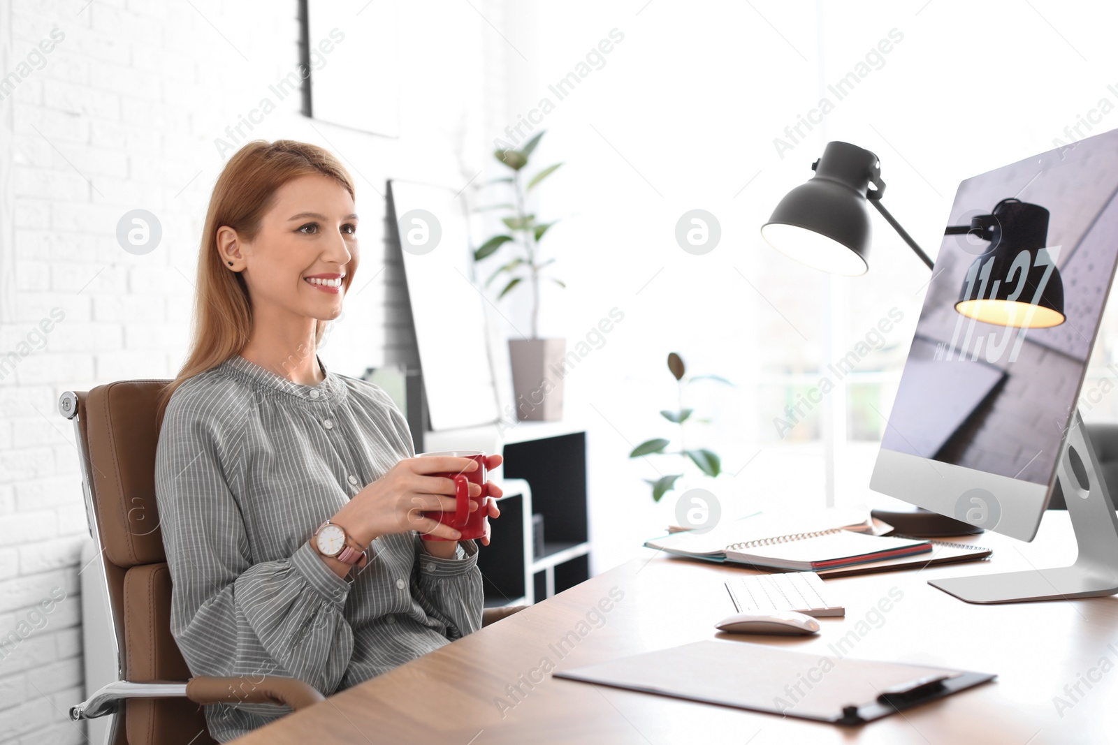 Photo of Young woman with cup of drink relaxing at table in office during break