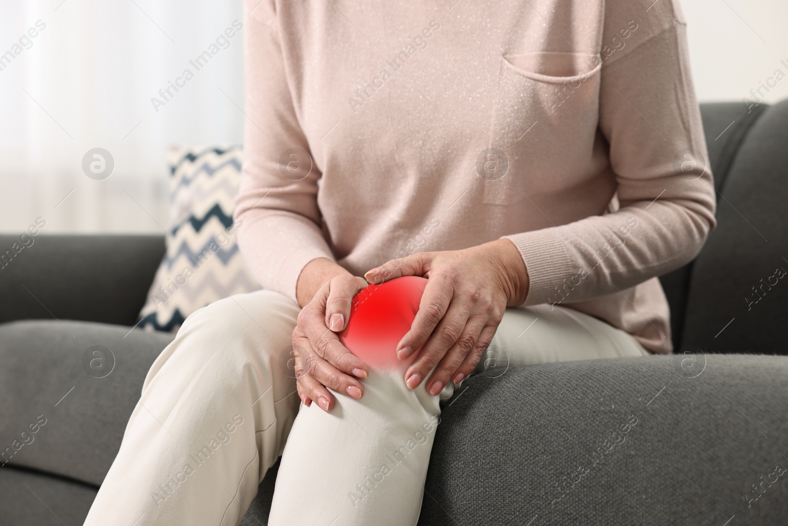 Image of Woman suffering from pain in knee on sofa indoors, closeup