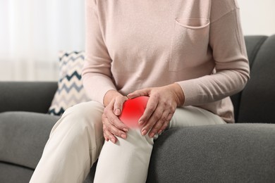 Woman suffering from pain in knee on sofa indoors, closeup