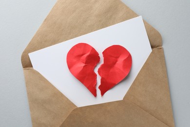 Photo of Envelope with halves of torn red paper heart on white background, top view. Broken heart