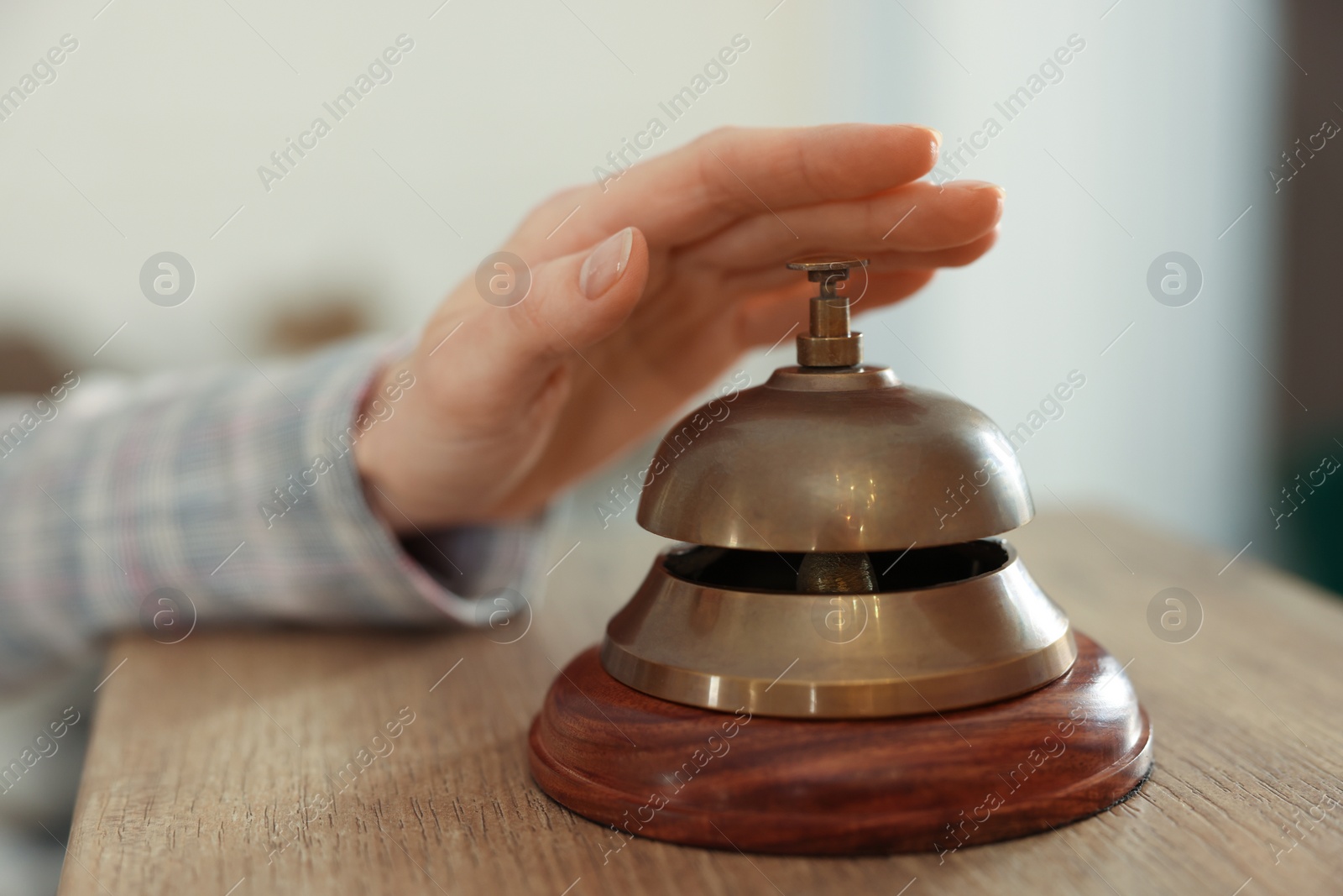 Photo of Woman ringing hotel service bell at wooden reception desk, closeup