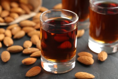 Photo of Glasses with tasty amaretto liqueur and almonds on dark gray table, closeup