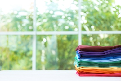 Photo of Stack of bright folded clothes on table against blurred background. Space for text