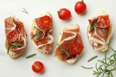 Photo of Tasty sandwiches with cured ham, rosemary and tomatoes on white marble table, flat lay