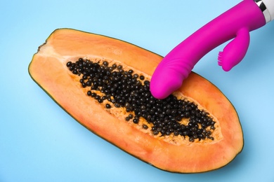 Half of papaya and purple vibrator on blue background, top view. Sex concept