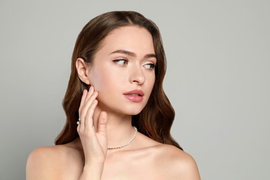 Young woman wearing elegant pearl jewelry on grey background, space for text