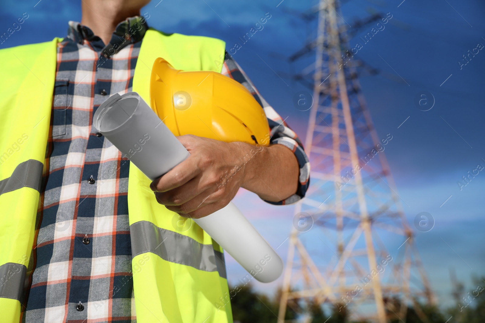 Photo of Professional electrician with drafting and helmet near high voltage tower, closeup