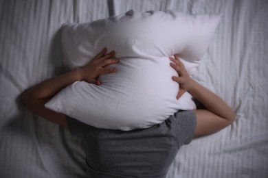 Woman covering her head with pillow on bed, top view. Insomnia problem