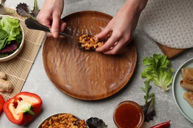 Photo of Woman making tasty spring roll at grey table, top view