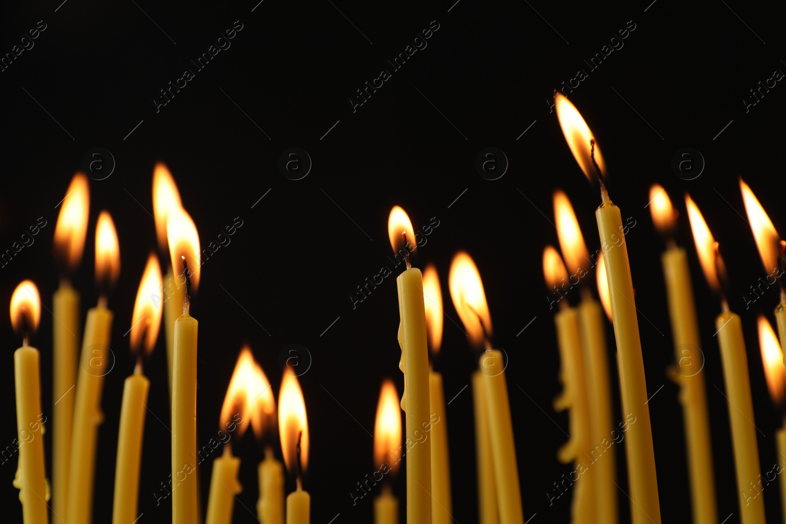 Photo of Many burning church candles on black background