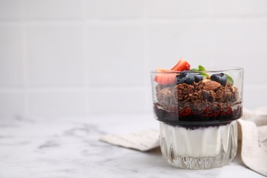 Photo of Tasty granola with berries, jam and yogurt in glass on white marble table, space for text