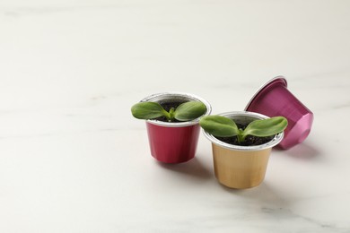 Photo of Coffee capsules with seedlings on white marble table, space for text