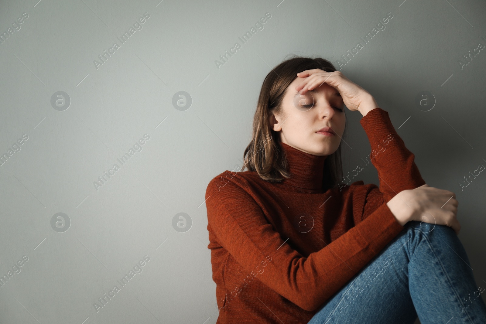 Photo of Sad young woman near grey wall, space for text